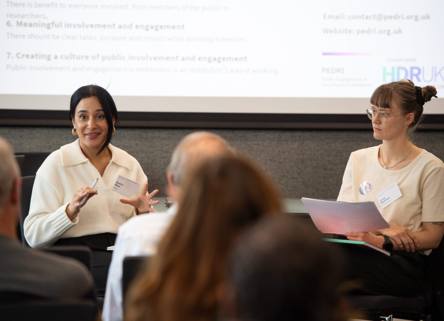 Two people are sitting down talking to each other in front of a crowd.