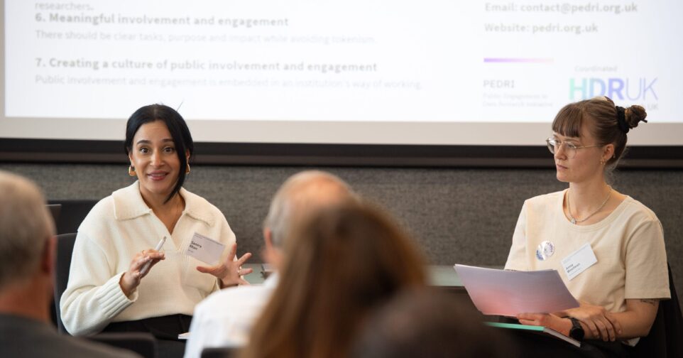 Two people are sitting down talking to each other in front of a crowd.