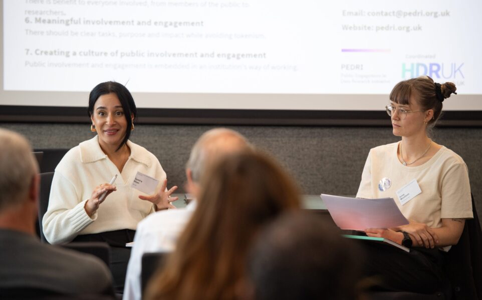 Two people are sitting down talking to each other in front of a crowd.