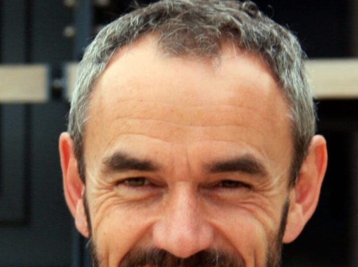 A man with dark grey hair and a short dark beard smiling at the camera