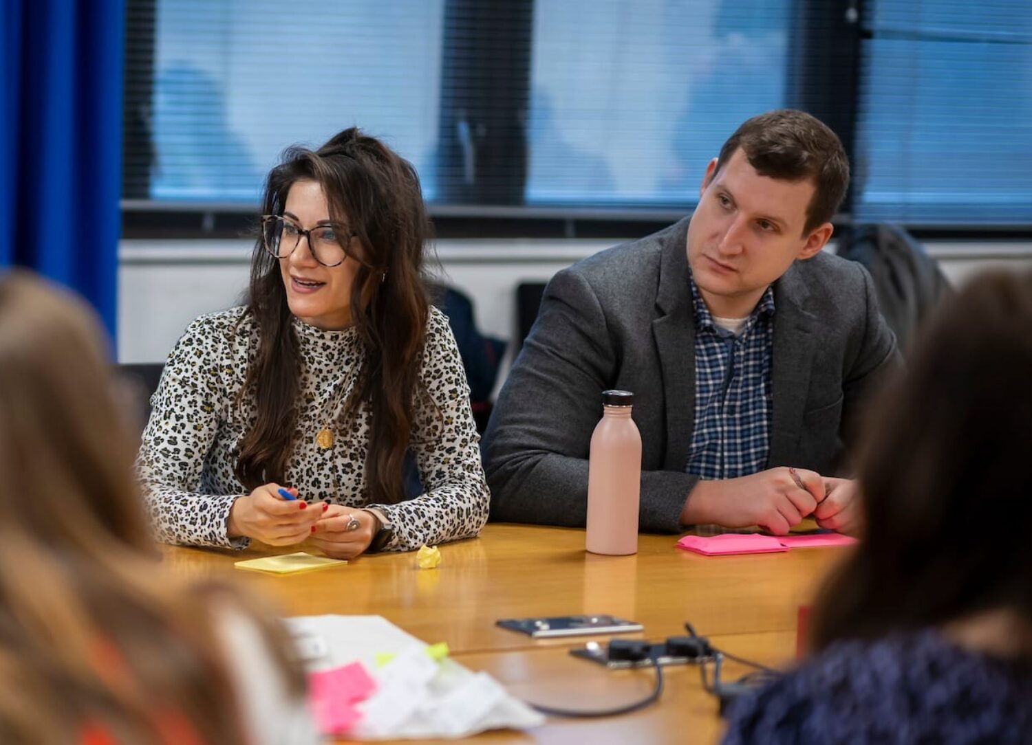 Two people sit at a table looking in the same direction.