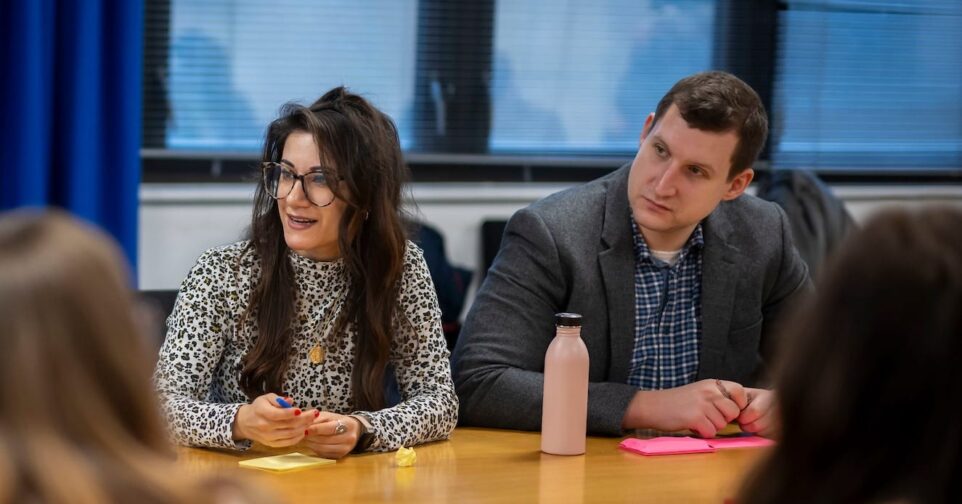 Two people sit at a table looking in the same direction.