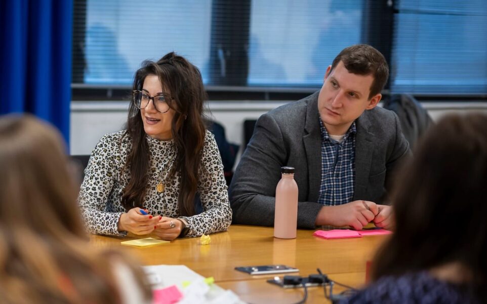 Two people sit at a table looking in the same direction.