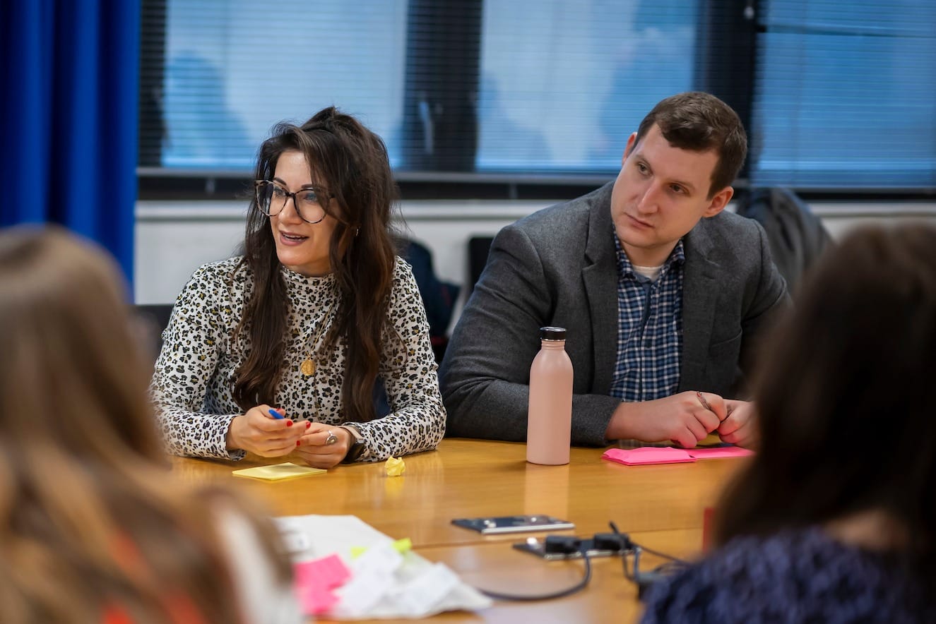 Two people sit at a table looking in the same direction.