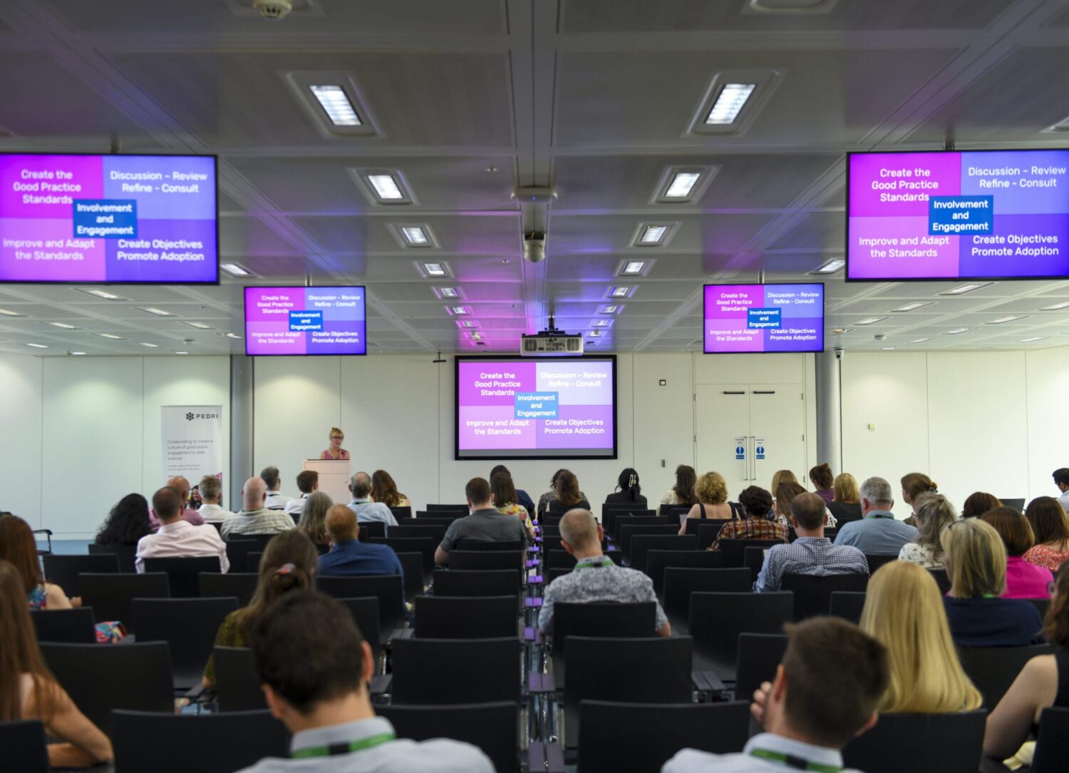 People sat in rows watching a speaker present a slide.