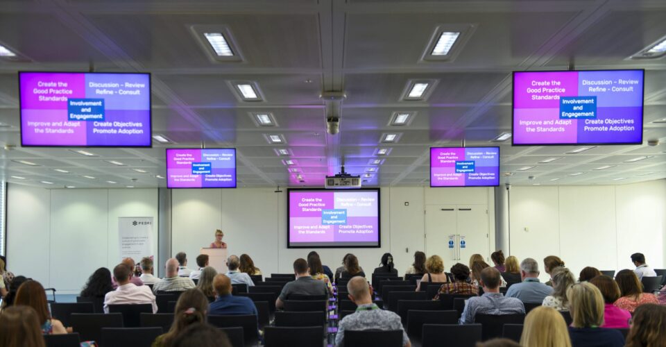 People sat in rows watching a speaker present a slide.