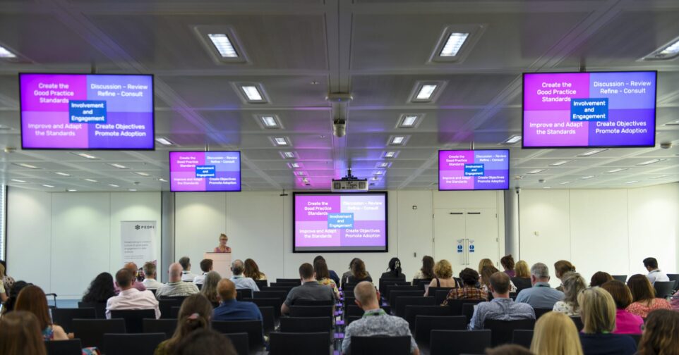 People sat in rows watching a speaker present a slide.