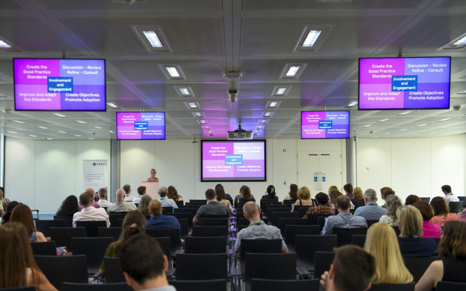 People sat in rows watching a speaker present a slide.