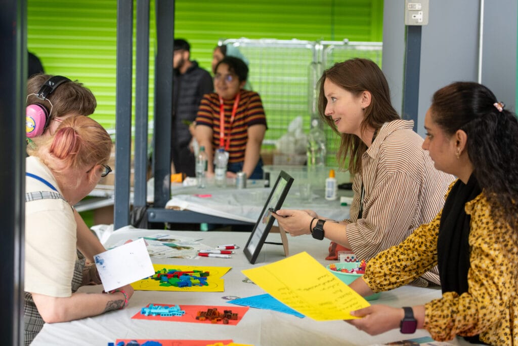 Two women speaking to parent and child across a desk with lego on it.