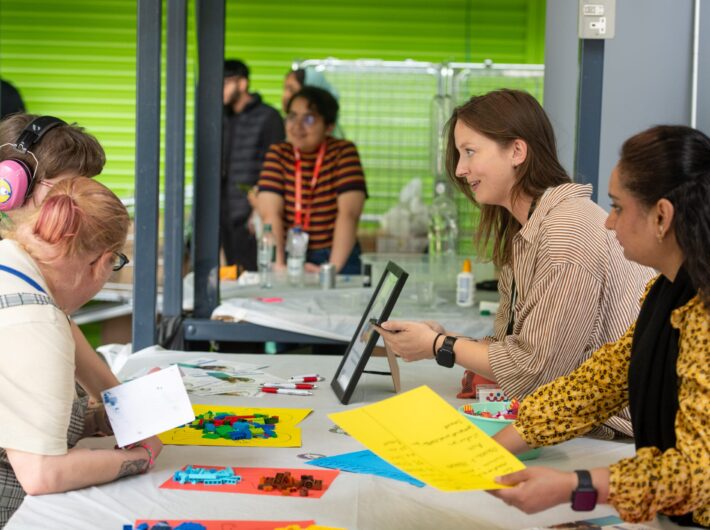 Two women speaking to parent and child across a desk with lego on it.