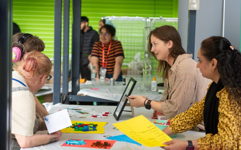 Two women speaking to parent and child across a desk with lego on it.