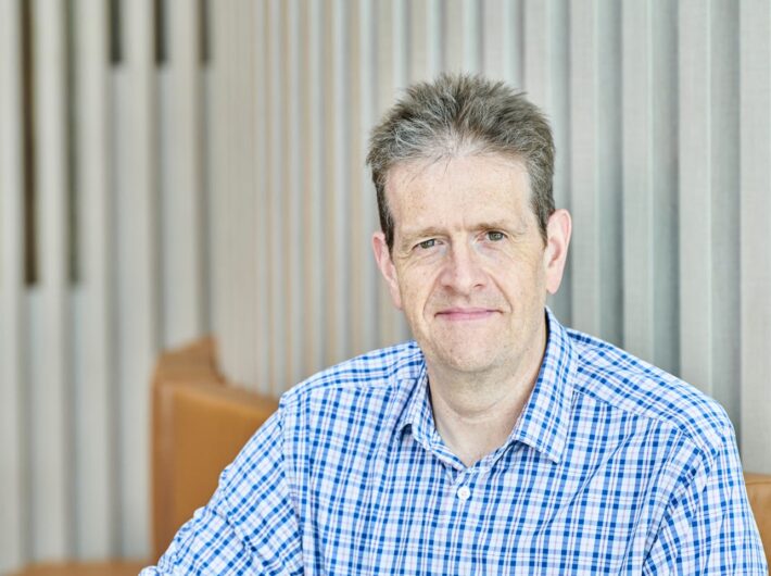 A person with short hair and a blue checkered shirt smiles at the camera