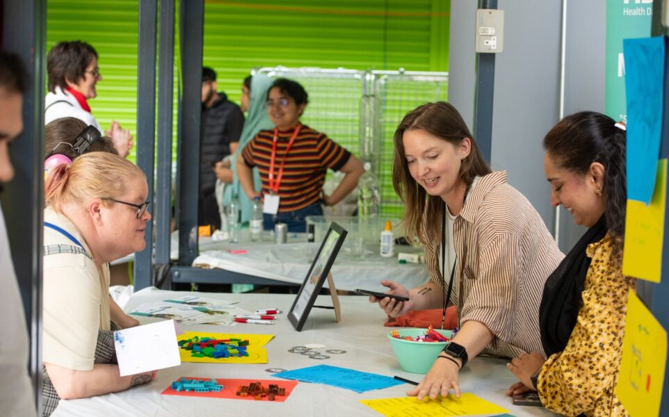 3 women stood around table talking and looking at different colour cards