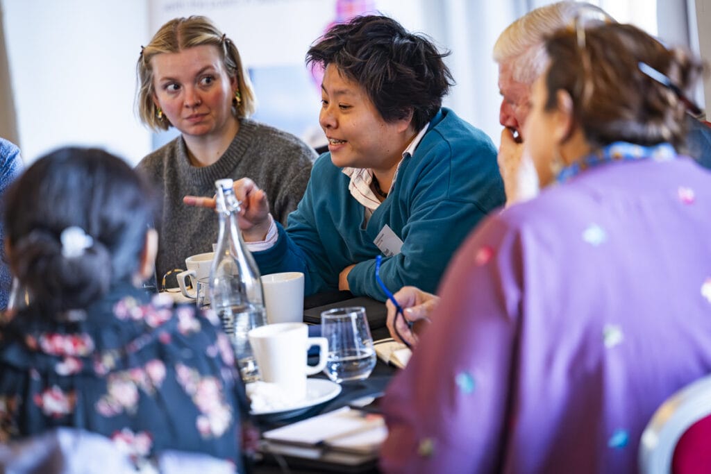 group of people sat round table with one person talking