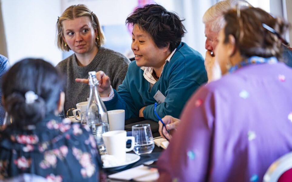 group of people sat round table with one person talking