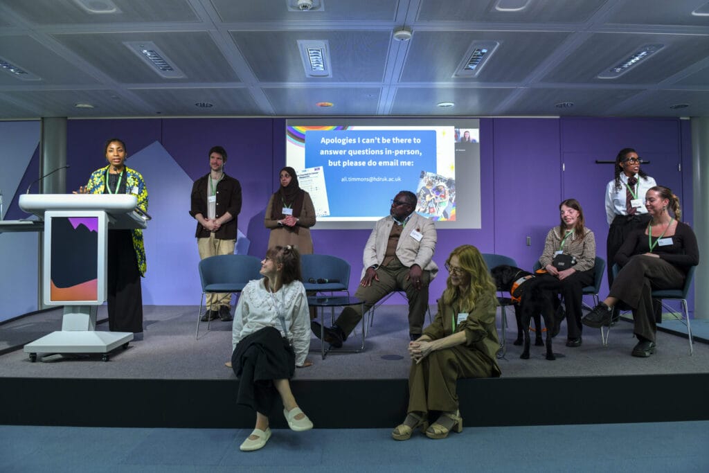 Group of people standing and sitting on lecture theatre stage.